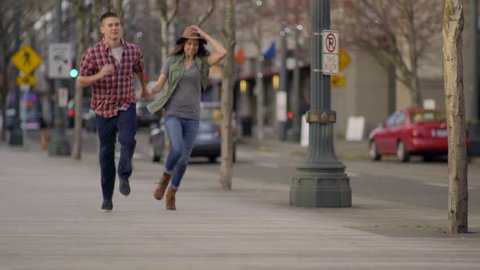 Adventurous Young Couple Hold Hands And Run (Toward Camera) In The City 