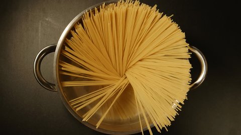 TOP VIEW: A cook puts down a spaghetti in a steel pot (round)
