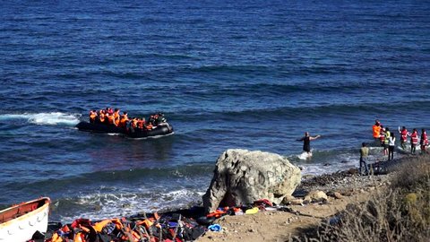 Refugees swim up to the coast by the boat. Lesbos, Greece. October 14, 2015. A dangerous and illegal way through the sea from Turkey to the Europe. People help them to get out of the boat ashore.