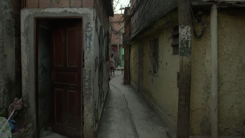 Rio de Janeiro, Brazil - CIRCA February 2014: View of an alley in a poor neighbourhood. There is a wooden door at one of the apartment and a woman standing in the background with her kid.