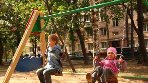 Boy and little girl sway on swing at playground