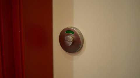 Close-up of a public toilet door lock which is green indicating cubicle is empty. Man opens door, enters, closes door and turns lock to red indicating cubicle is occupied or busy.