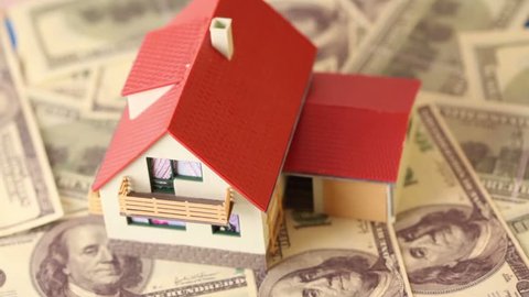 Toy house with red tiled roof on dollars bank notes, composition rotates