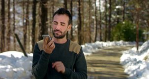 young beautiful and elegant man filmed while phoning with a smart phone happily with friends or someone in a connection world, more precisely in a forest at the foot of mountain. connectivity concept