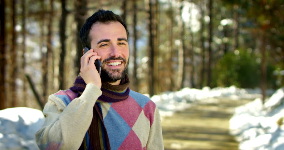 young beautiful and elegant man filmed while phoning with a smart phone happily with friends or someone in a pleasant natural environment , more precisely in a forest at the foot of a mountain