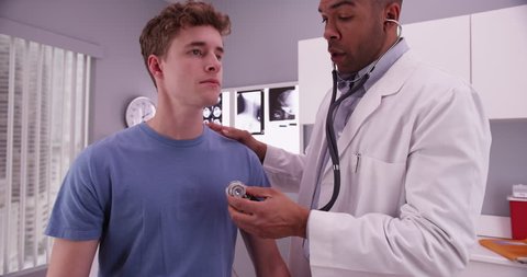 African-american doctor using stethoscope to listen to lungs of male caucasian patient