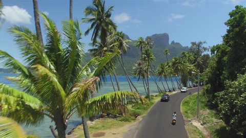4K AERIAL: Young woman riding motorbike on beautiful Bora Bora island resort on sunny summer vacation