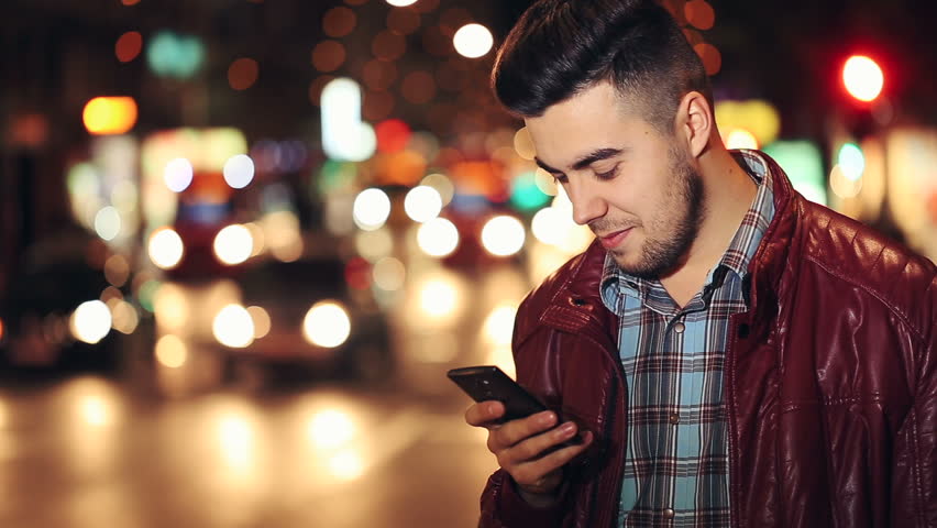 Man sms texting using app on smart phone at night in city