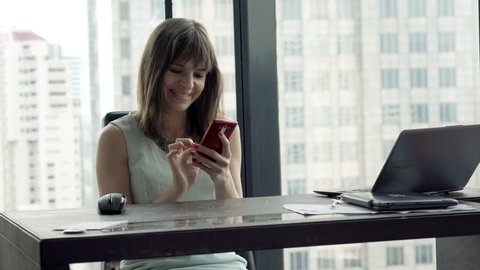 Happy, young businesswoman using smartphone in office
