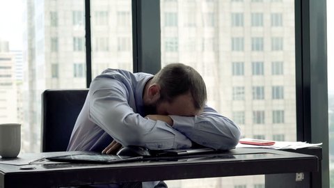 Tired businessman with laptop falling asleep in office 
