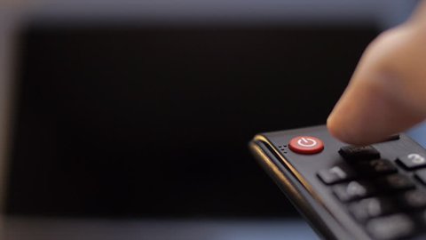 Hand turns on the TV and switch the channels by remote control then turn off the device. Remote control at the background of the screen TV panels. Closeup. Shallow depth of field