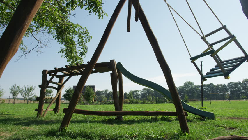 An empty wooden swing rocks back and forth on a farm in the summer. Closeup. 4k.
