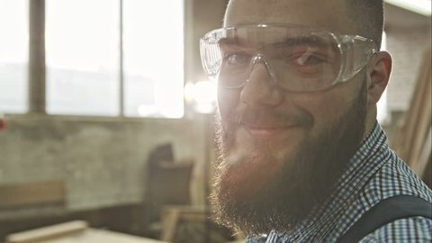 Closeup view of one handsome young adult man worker with a beard and goggles. RAW video record.