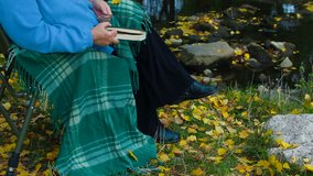 elderly woman sitting in a chair at autumn park reading book, Unrecognizable Person,  Side View