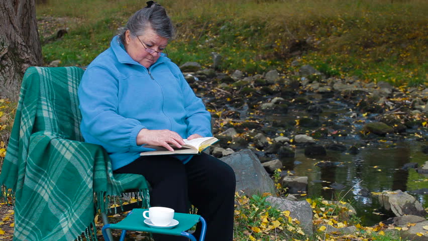 Elderly woman reading a book with a cup of coffee in the park.