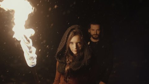 Portrait of a young mystic couple holding a torch in the dark forest. Mystery couple in the woods. Snowing. Slow motion.