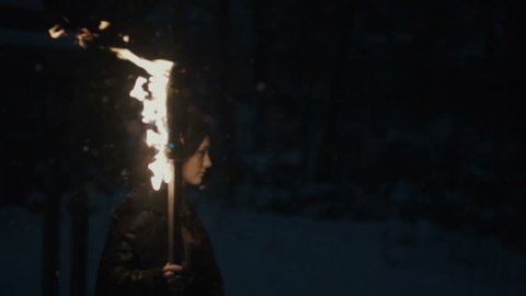 Portrait of a young mystic woman walking in the dark forest with a torch. Young woman with torch over dark night background. Slow motion. Winter season.