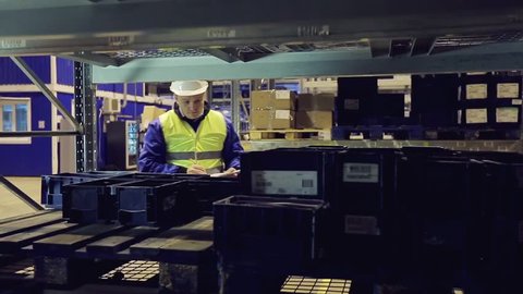 Worker in uniform going along shelves and checking cargo