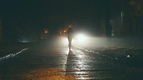 Girl at night is on the dangerous streets of the city on the car headlights.