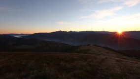 The first rays of rising sun in autumn Carpathian Mountains. Video has view of rural road on ridge, mountain tops and mist between the mountain slopes. There is some sun flare effect.
