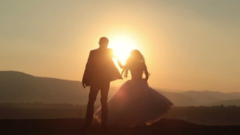 Silhouettes of wedding couple gracefully dances in the mountains