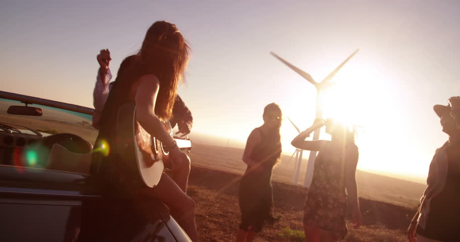 Caucasian young adult woman playing guitar oudoor on a summer sunset with friends and sings