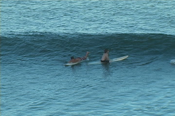 A surfer wipes out and lands in the path of another surfer causing him to fall