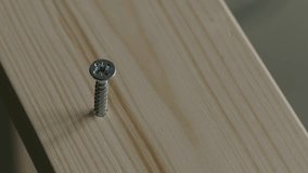 Ungraded: DIY furniture assembly. Craftsman drives the screw into the untreated unpainted wooden board with an electric powered screwdriver. Macro close-up. Source: Lumix DMC, ungraded. (av26023u)