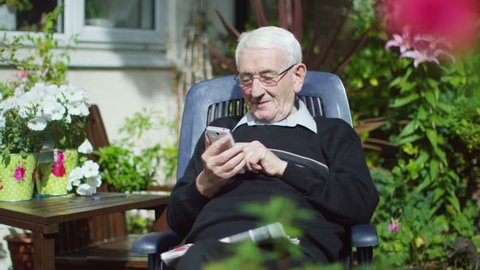 4K Portrait of elderly man sitting alone making mobile phone call in the garden
