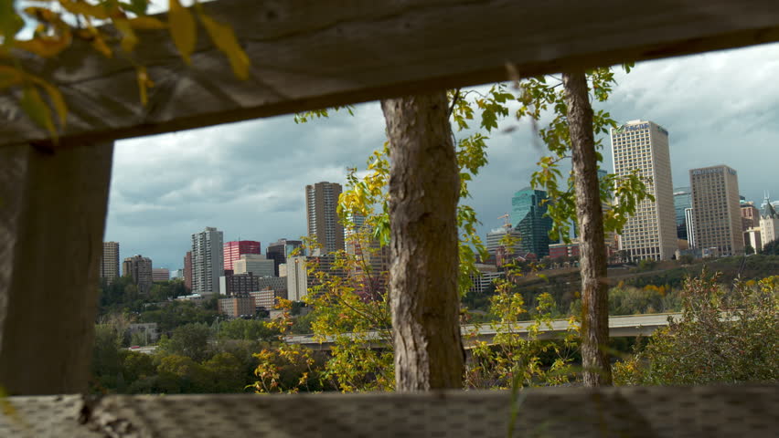 Slider shot of the capital city of Edmonton in Alberta, Canada with wooden fence and foliage in the foreground.  Skyline shot of downtown.