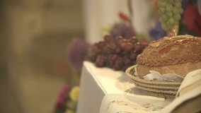 Panning shot of bread and grapes on table. Priest shaking incense in background. Food of life during wedding ceremony. Bread and grapes on table during wedding ceremony


