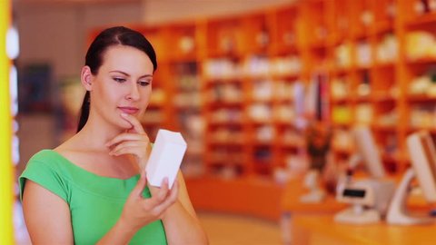Pensive young woman looking at medical product in pharmacy
