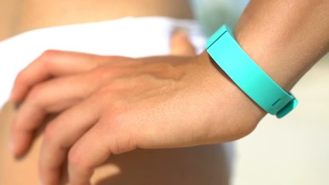 Young woman standing with hand on hip at beach. Fit runner is wearing turquoise colored activity fitness tracker watch on sunny day. Female is in white bikini bottom.