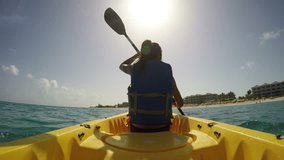 Young woman kayaking on sea against sky during sunny day. Female is on her summer vacations at beach. She is wearing life jacket while paddling the kayak. ACTION CAMERA.