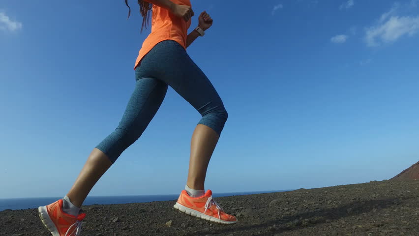 Running woman outdoors on run. Fast female runner running shoes and legs close up on mountain trail. Female is in sportswear. Fitness woman exercising in nature on sunny day. ACTION CAMERA.