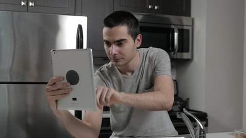 Young man in a home kitchen using his tablet device.