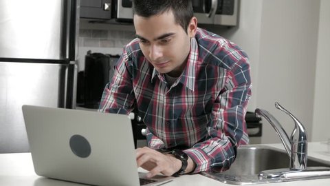 Young man in a home kitchen using a laptop computer
