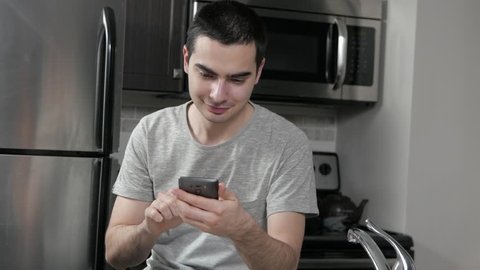 Young man in a home kitchen using a smartphone device.