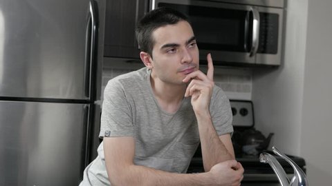 Young man in a home kitchen thinking.