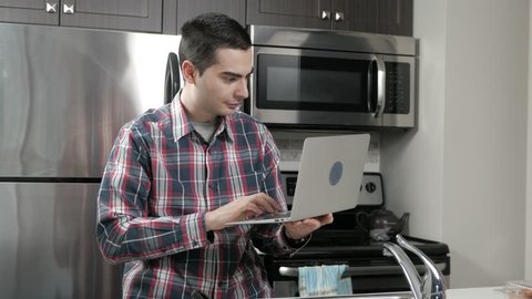 Young man in a home kitchen using a laptop computer