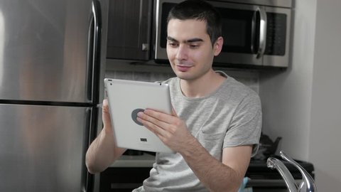 Young man in a home kitchen using his tablet device.