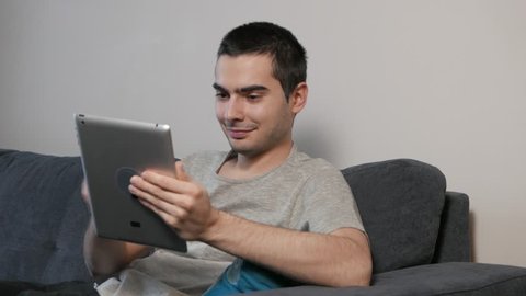 Sitting on a couch and using a tablet device.