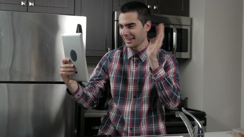 Young man in a home kitchen talking trough video chat (facetime) to somebody.