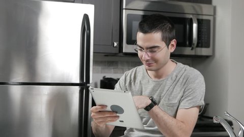 Young man in a home kitchen using a tablet to shop with his credit card.