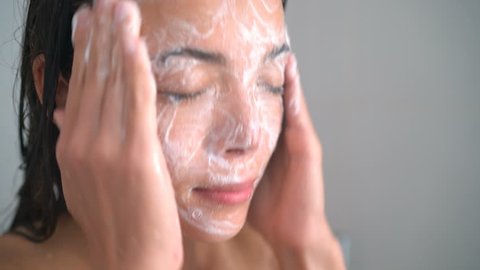 Skincare woman washing scrubbing face with facewash soap scrub in hot water shower. Closeup of Asian female young adult face cleaning skin.