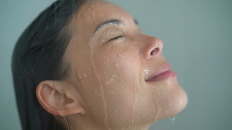 Spa woman showering relaxing under running water in hot shower. Closeup of Asian female adult face enjoying relaxation time meditating in warm bath cleaning face and body.