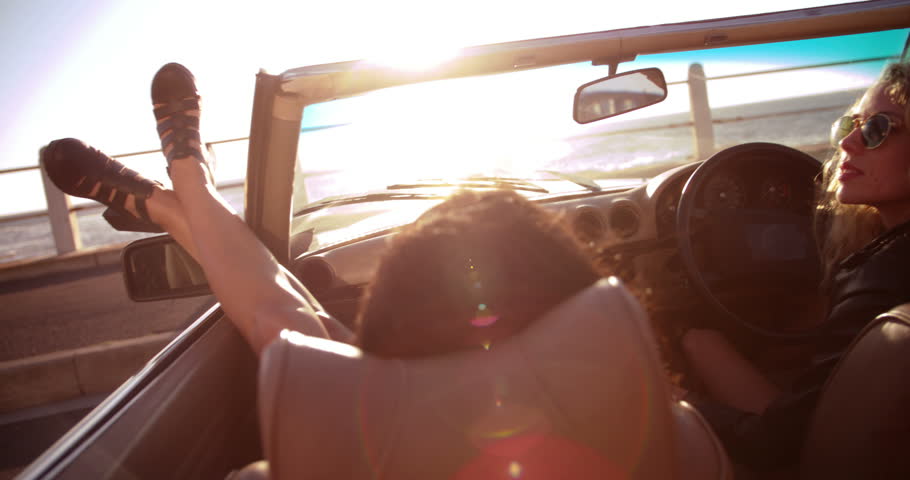 Two young women enjoying a summer sunset on seaside sitting in a vintage convertible with sunflare | Shutterstock HD Video #15173233