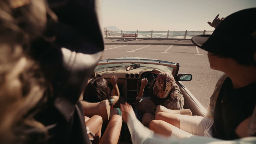 Group of multi-ethnic hipster friends embracing each other joyfully on promenade watching the sea