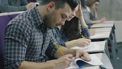 Footage of students writing with pens on paper in a collage classroom during lecture. Shot on RED Cinema Camera in 4K (UHD).