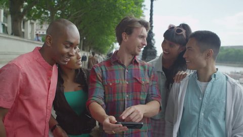 4K Portrait of happy mixed ethnicity group of friends looking at smartphone outdoors
